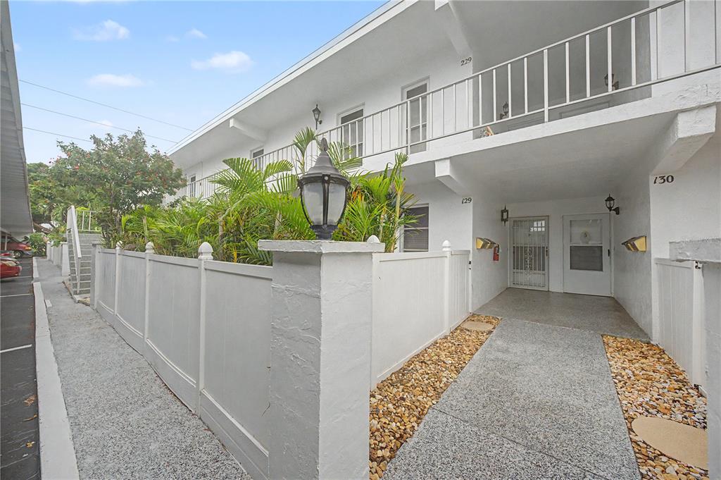 Exterior view of a two-story white apartment building with a fenced patio and walkway — 1655 S HIGHLAND AVENUE UNIT F129, CLEARWATER, FL