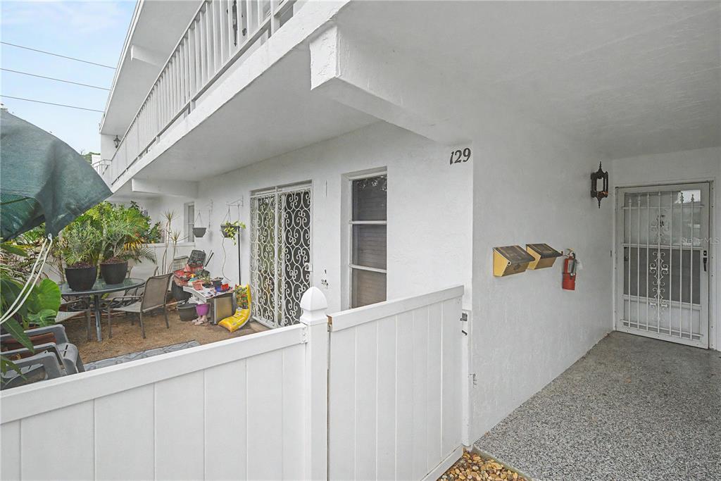 An exterior view of a ground-floor apartment entrance with a small patio and white fence — 1655 S HIGHLAND AVENUE UNIT F129, CLEARWATER, FL