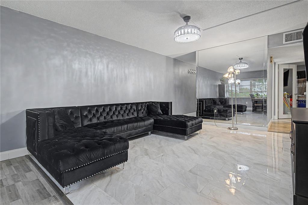 A living room features a black tufted sectional sofa, light marble flooring, and a mirrored wall — 1655 S HIGHLAND AVENUE UNIT F129, CLEARWATER, FL
