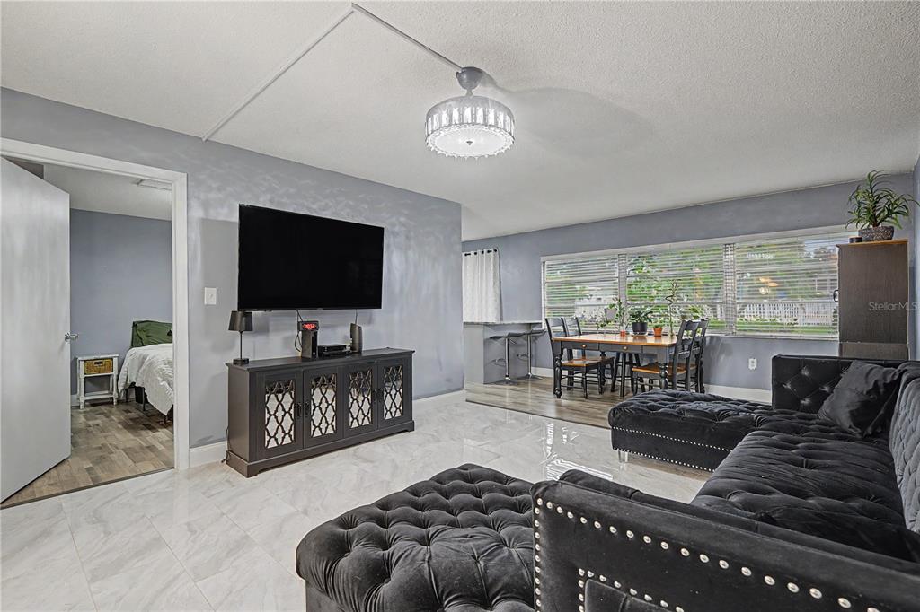 A living room features light gray walls, white tile flooring, a black sectional, and a television — 1655 S HIGHLAND AVENUE UNIT F129, CLEARWATER, FL
