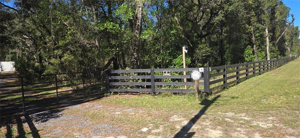 A black wooden fence borders a wooded lot with a gated gravel driveway entrance — 11150 NW 78TH AVENUE, CHIEFLAND, FL