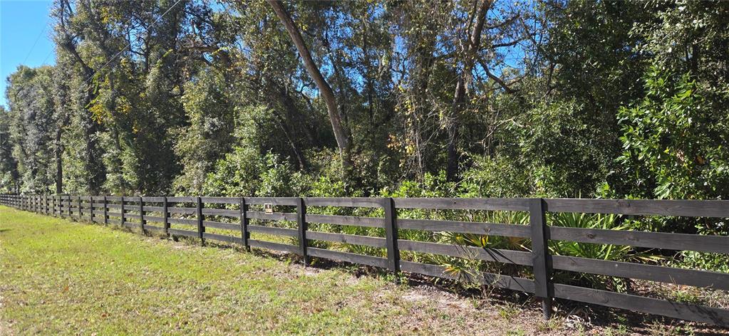 A black wooden fence runs along the edge of a grassy area in front of trees — 11150 NW 78TH AVENUE, CHIEFLAND, FL