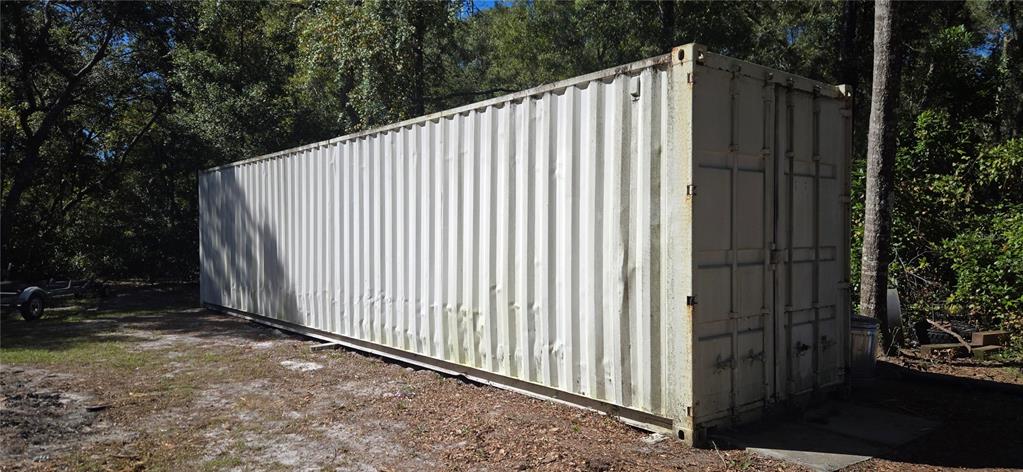 A white shipping container sits on a dirt lot surrounded by trees — 11150 NW 78TH AVENUE, CHIEFLAND, FL