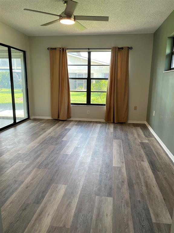 An empty room features wood-look vinyl flooring, a ceiling fan, and a sliding glass door — 3610 54TH STREET W UNIT B8, BRADENTON, FL