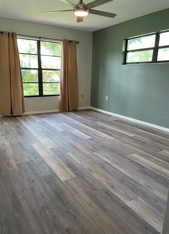 An empty bedroom features wood-look flooring, a ceiling fan, and an accent wall — 3610 54TH STREET W UNIT B8, BRADENTON, FL