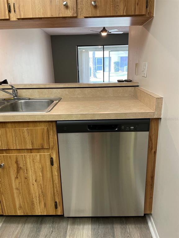 A kitchen features wood-grain cabinets, a stainless steel dishwasher, and a view into the living area — 3610 54TH STREET W UNIT B8, BRADENTON, FL