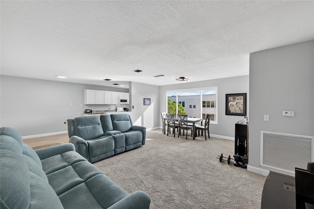 A living room with gray carpet, a blue sofa, and an adjacent dining area — 5521 80TH STREET N UNIT 511, ST PETERSBURG, FL