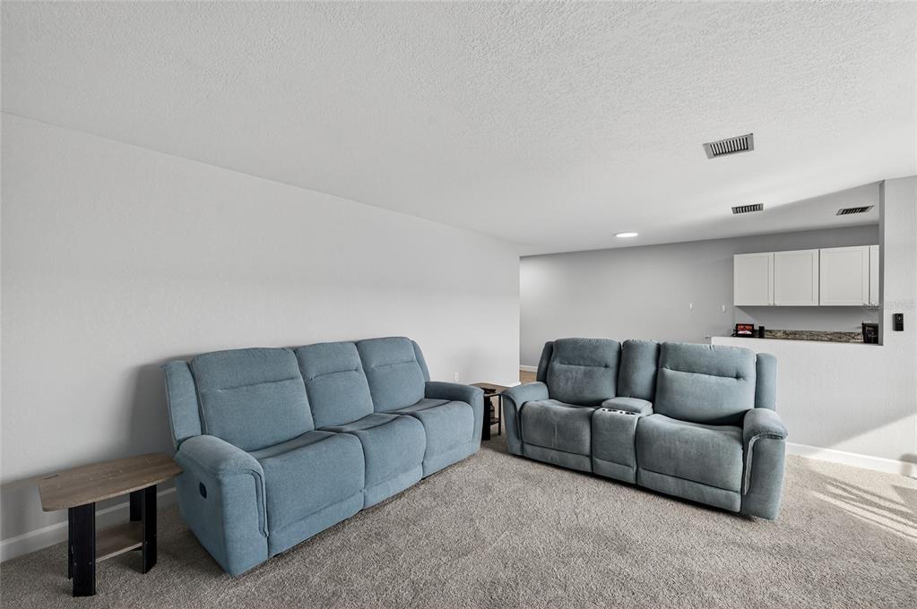 A living room features two blue reclining sofas on carpeted flooring near a kitchen counter — 5521 80TH STREET N UNIT 511, ST PETERSBURG, FL