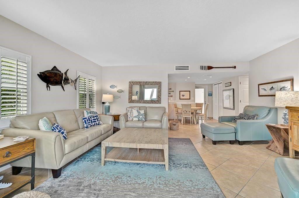 A living room with light-colored sofas, a wooden coffee table, and coastal-themed wall decor — 6154 MIDNIGHT PASS ROAD UNIT 206, SARASOTA, FL