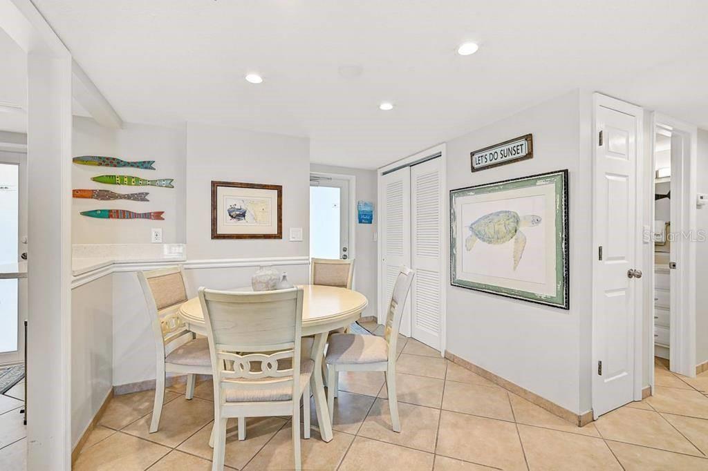 A dining area features a round table, four chairs, tile flooring, and coastal wall decor — 6154 MIDNIGHT PASS ROAD UNIT 206, SARASOTA, FL