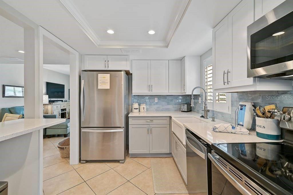 A kitchen features white cabinets, stainless steel appliances, a farmhouse sink, and light blue backsplash — 6154 MIDNIGHT PASS ROAD UNIT 206, SARASOTA, FL