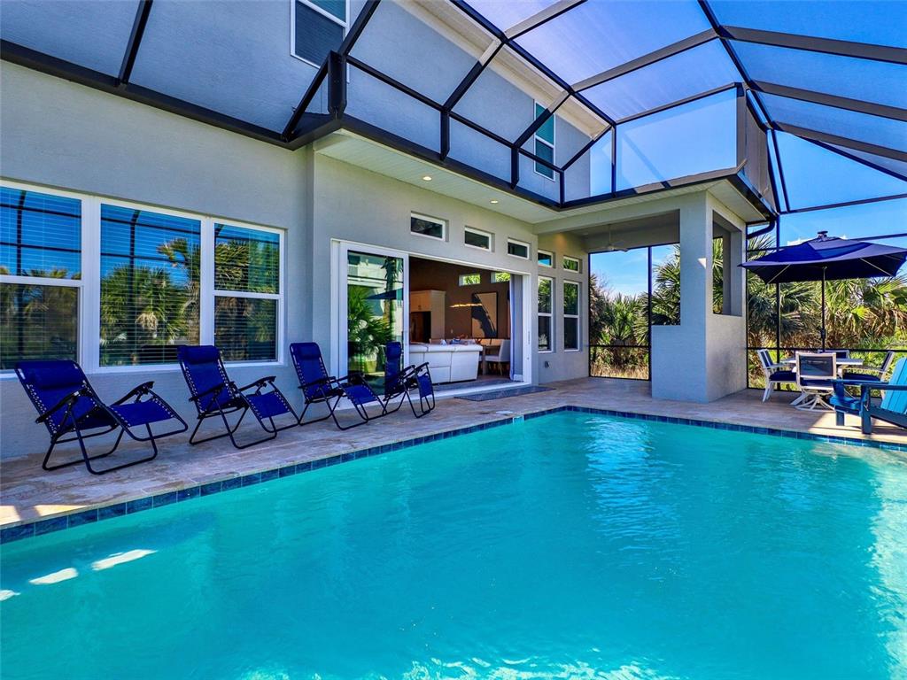 A swimming pool sits on a patio enclosed by a screen cage behind a house — 55 ATLANTIC DRIVE, PALM COAST, FL