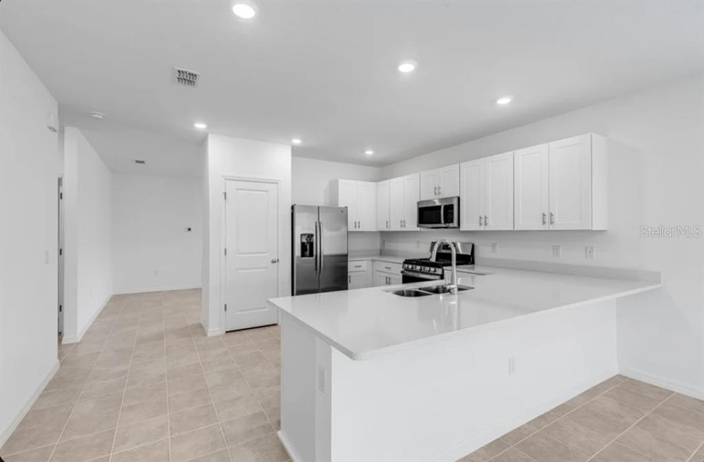 A modern kitchen features white cabinets, stainless steel appliances, and a quartz-topped island — 9336 CHISWELL TRAIL, PALMETTO, FL