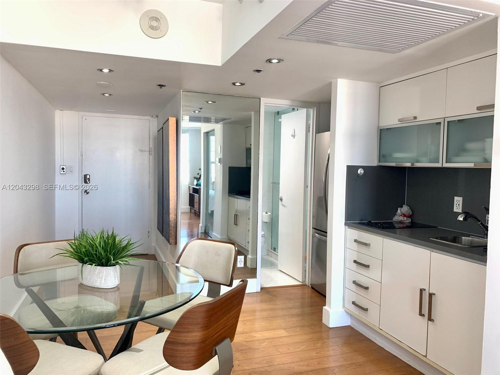 A dining area with a glass table sits adjacent to a kitchen with white cabinets — 100 Lincoln Rd # 1514A, Miami Beach FL 33139, MIAMI BEACH, FL