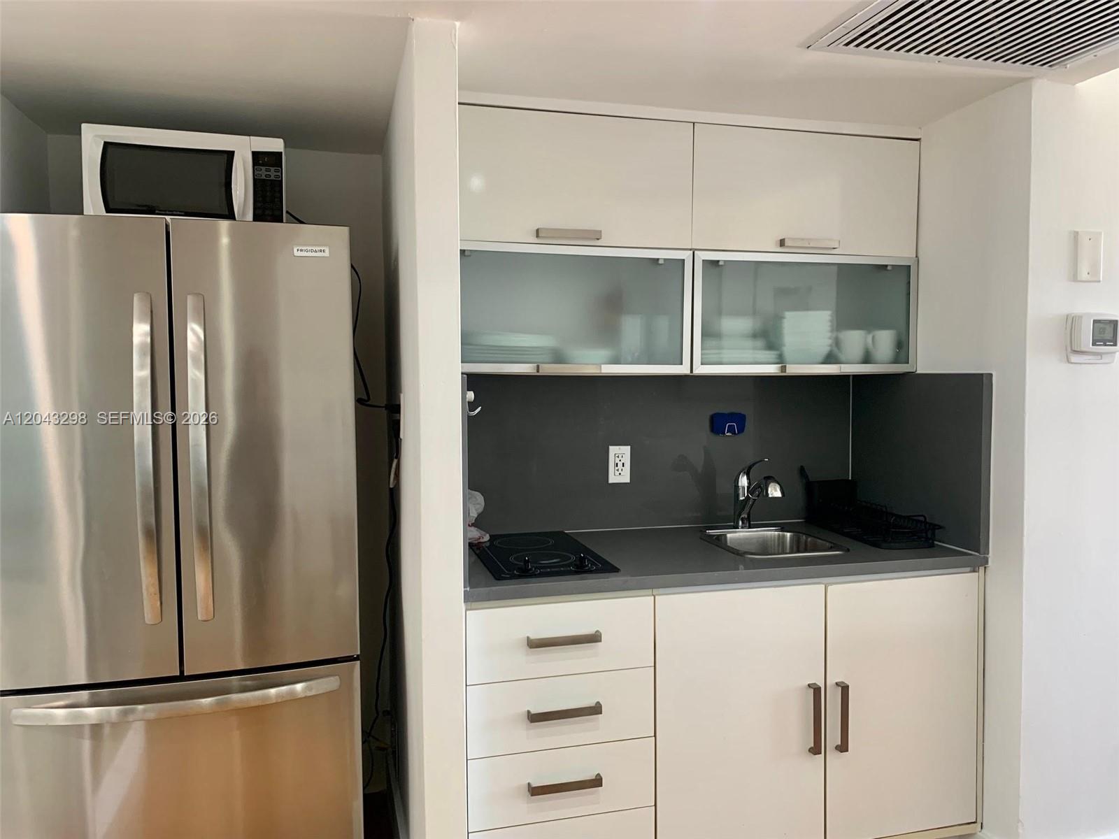 A small kitchen features stainless steel appliances, white cabinetry, and a gray countertop — 100 Lincoln Rd # 1514A, Miami Beach FL 33139, MIAMI BEACH, FL