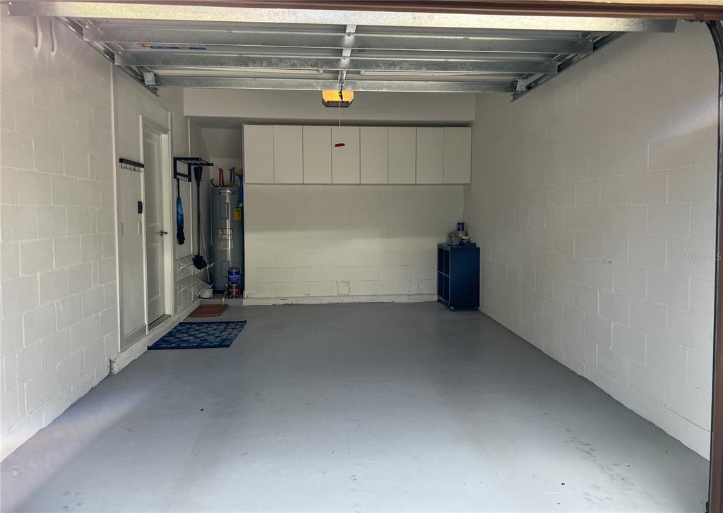 A clean, empty garage with white concrete block walls, gray painted floors, and overhead storage cabinets — 8984 AZALEA SANDS LANE UNIT 8984, DAVENPORT, FL