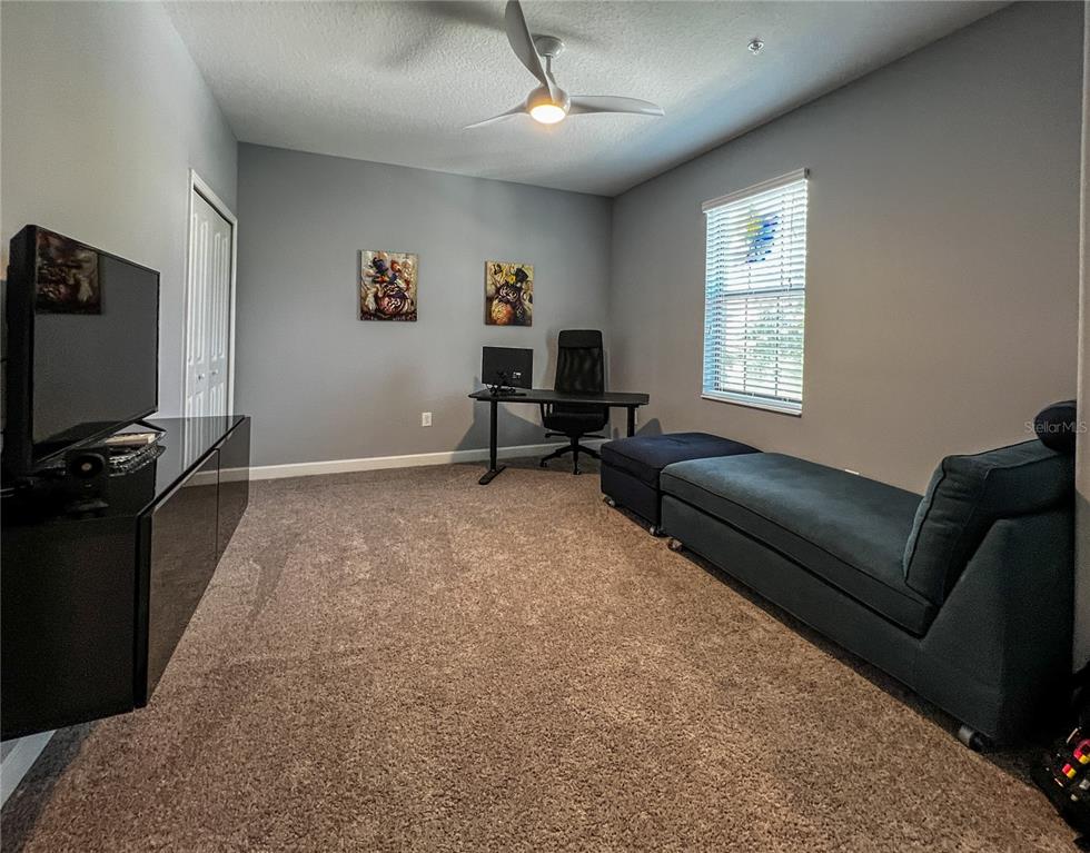 A carpeted room features a desk, a television on a console, and a chaise lounge — 8984 AZALEA SANDS LANE UNIT 8984, DAVENPORT, FL
