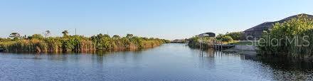 A canal view showing a grassy shoreline, a boat dock, and a nearby residential home — 10480 KINGSVILLE DRIVE, PORT CHARLOTTE, FL