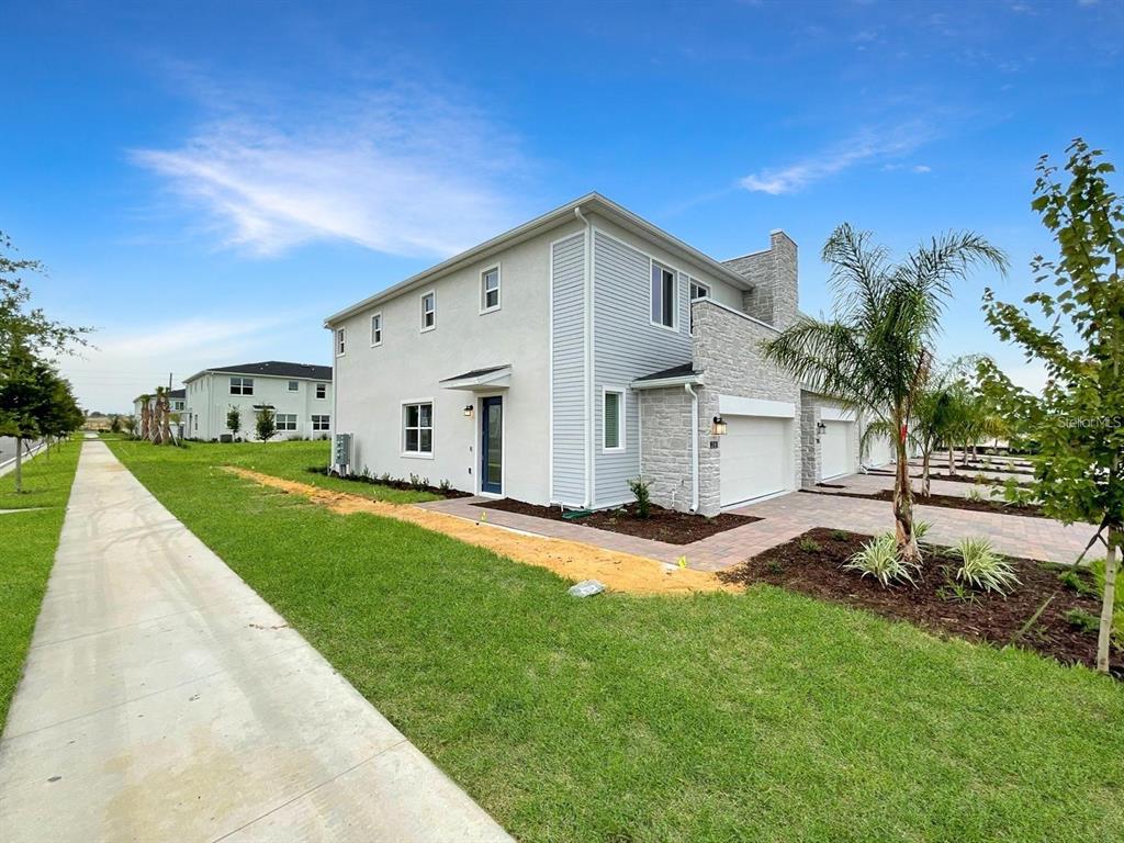 A two-story townhouse with a light gray exterior, stone accents, and a paved driveway — 218 NINE IRON DRIVE, DAVENPORT, FL