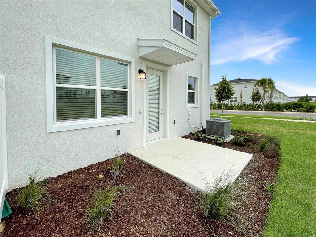 A white stucco house exterior features a small concrete patio, a door, and an AC unit — 218 NINE IRON DRIVE, DAVENPORT, FL