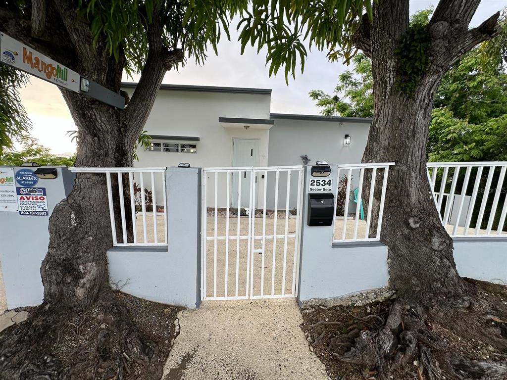 A white house with a gated entrance is framed by two large trees — Carr. 115 SECTOR SOTO ROAD, RINCON, PR