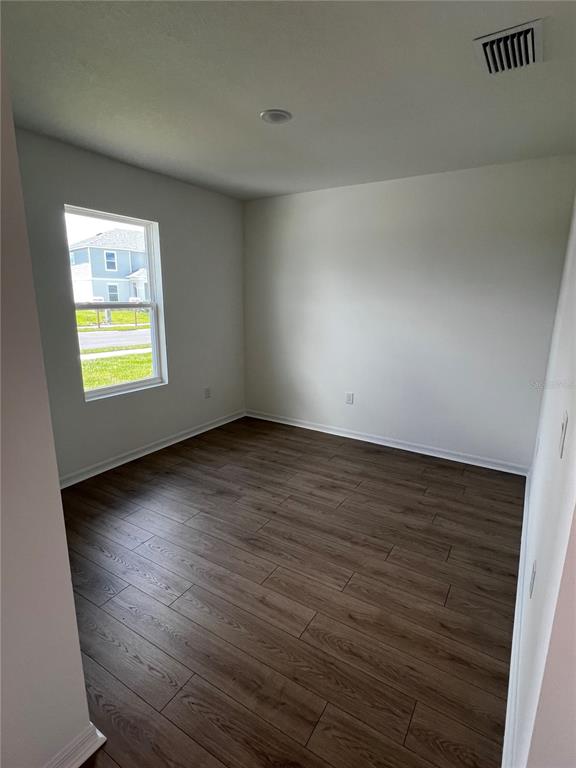 An empty room features wood-look tile flooring, white walls, and a window overlooking a neighborhood — 12918 RED DEER PLACE, PARRISH, FL