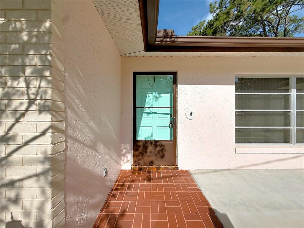 A front entryway features a light blue door, a storm door, and red brick flooring — 609 GOODYEAR AVENUE, INVERNESS, FL