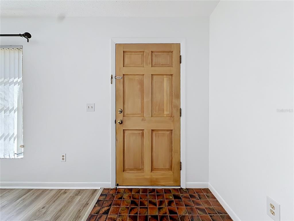 An interior view shows a wooden six-panel front door with tile flooring and white walls — 609 GOODYEAR AVENUE, INVERNESS, FL