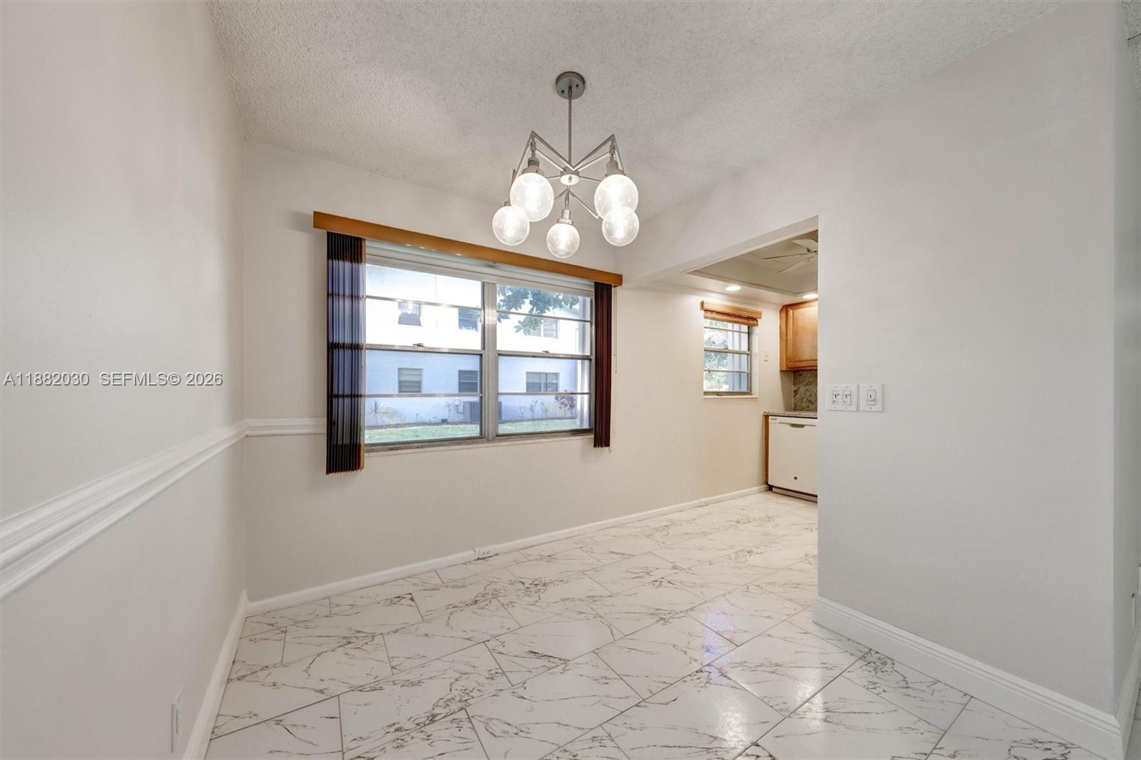 A dining area features white marble-look tile flooring, a modern chandelier, and a large window — 36 Islewood B # 36, Deerfield Beach FL 33442, DEERFIELD BEACH, FL