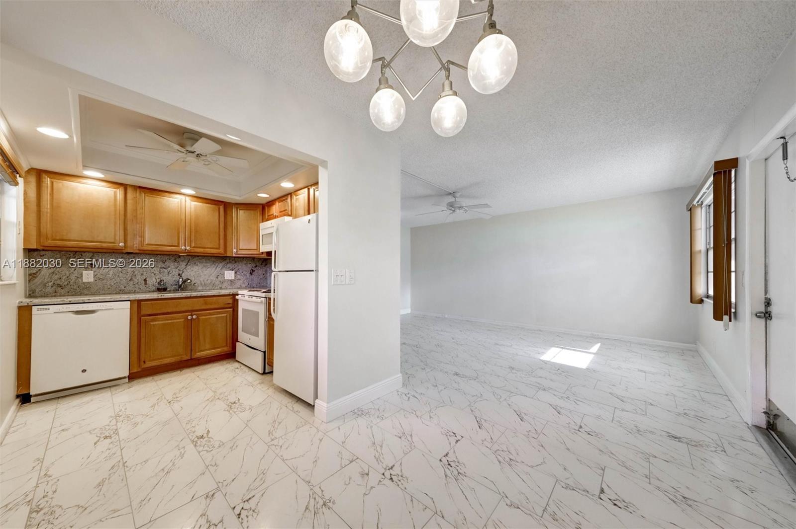 A kitchen with wood cabinets and white appliances opens into a dining area with tile — 36 Islewood B # 36, Deerfield Beach FL 33442, DEERFIELD BEACH, FL