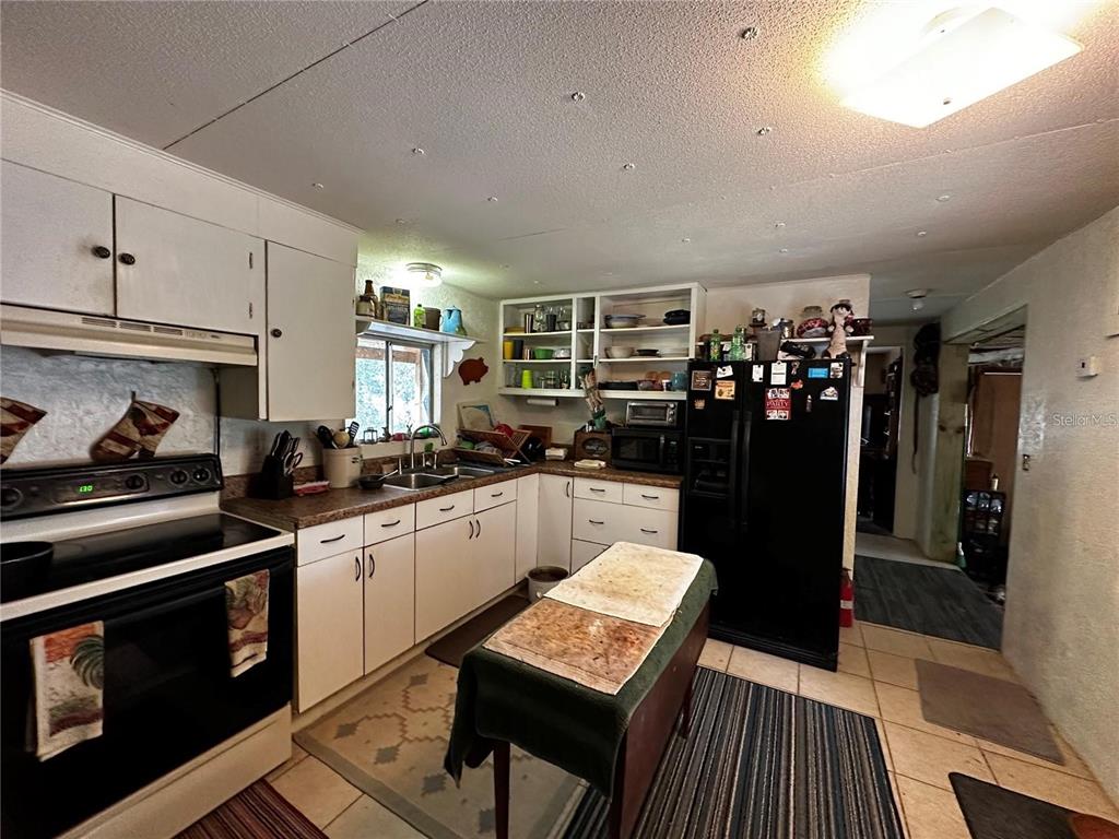 A kitchen features white cabinets, a black refrigerator, a stove, and a small central island — 12212 NE 238TH TERRACE, SALT SPRINGS, FL