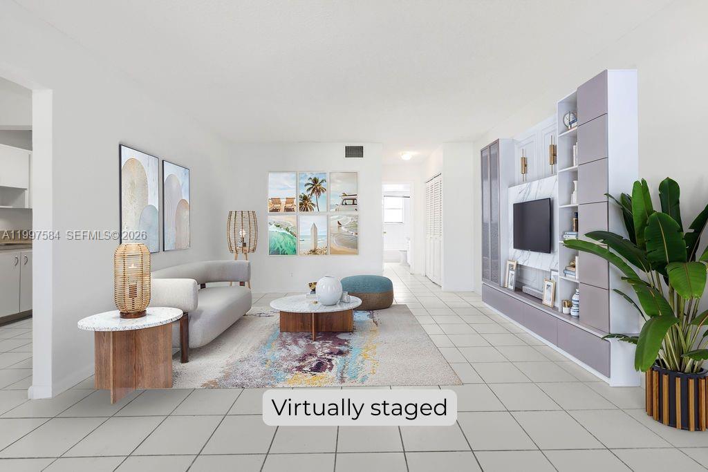 This virtually staged living room features white tile floors, a modern media unit, and artwork — 500 NE 2nd St # 223, Dania Beach FL 33004, DANIA BEACH, FL