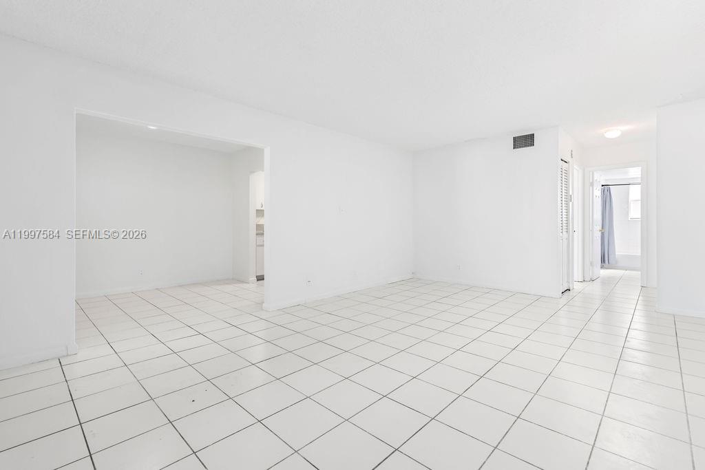 An empty room with white walls and white tile flooring leads to a hallway — 500 NE 2nd St # 223, Dania Beach FL 33004, DANIA BEACH, FL