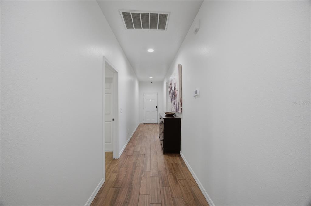 A long hallway features wood-look tile flooring, white walls, and a dark wooden console table — 8205 N 12TH STREET, TAMPA, FL