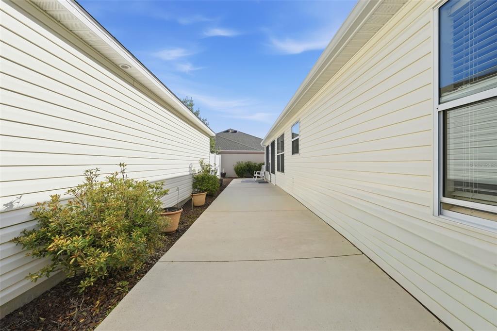 A concrete walkway sits between the side walls of two light-colored vinyl-sided houses — 2311 CRESTVIEW STREET, THE VILLAGES, FL
