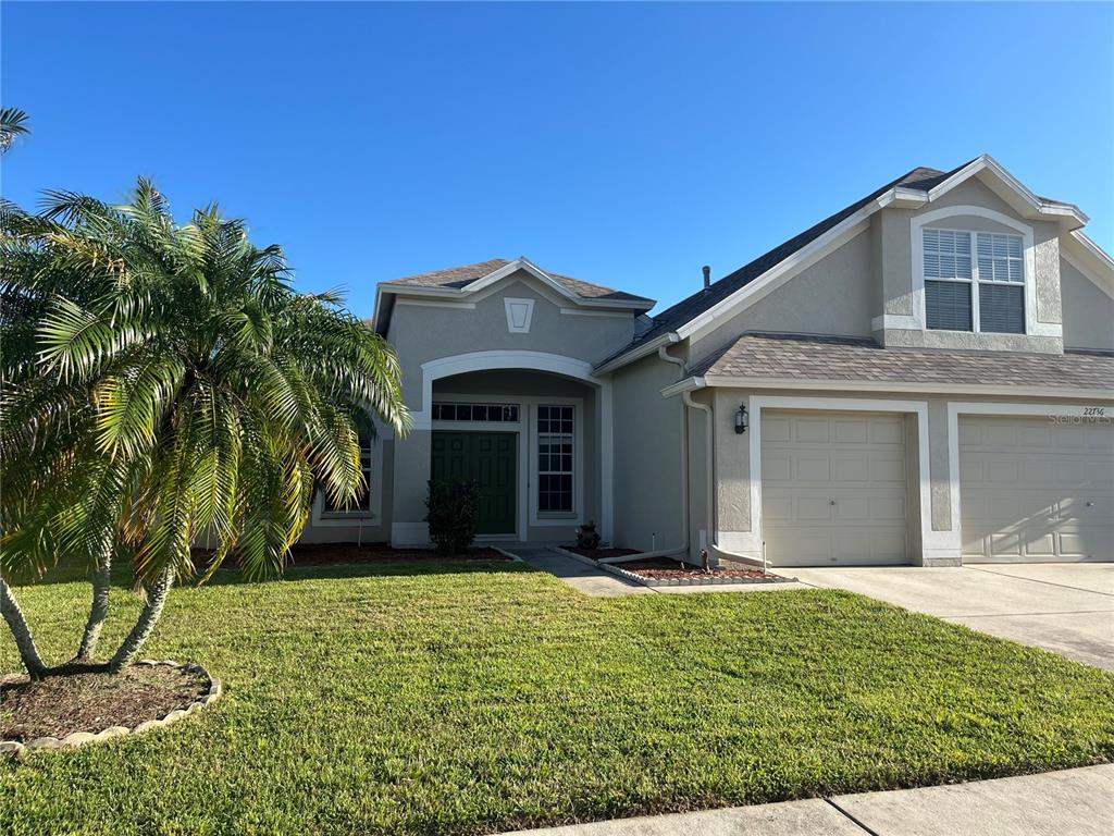 A single-story suburban house with a palm tree, a two-car garage, and a green front door — 22736 BELTREES COURT, LAND O LAKES, FL