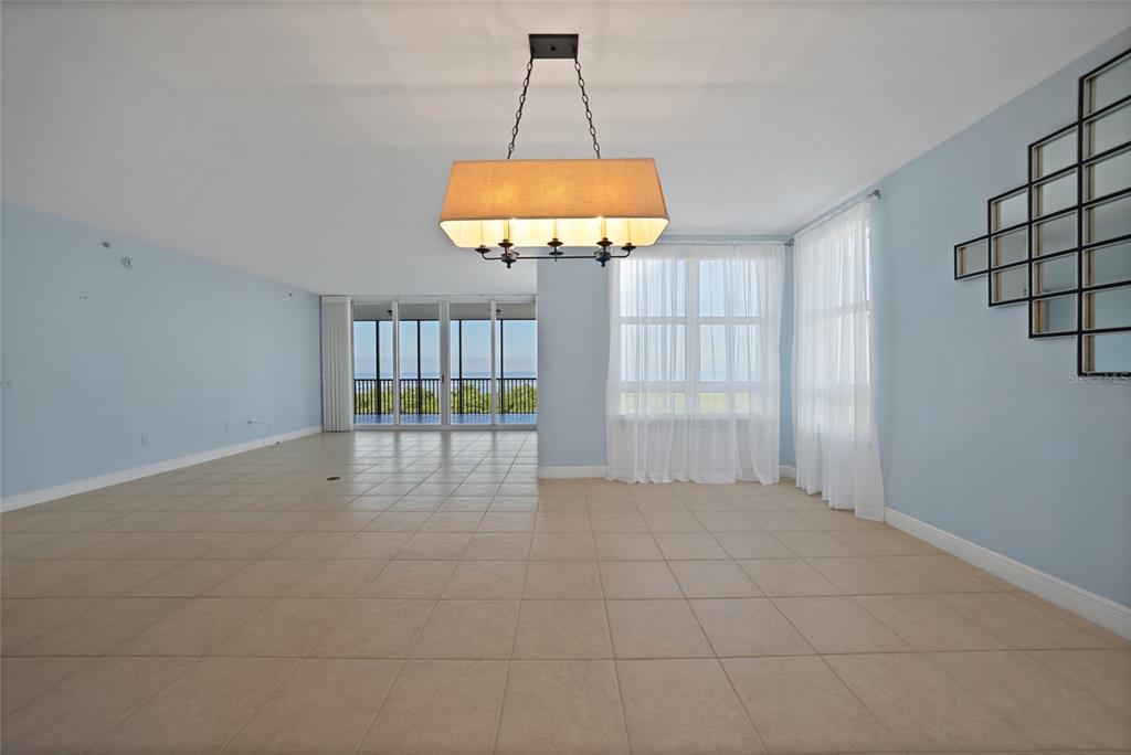 An empty living area with light blue walls, tile flooring, and a large rectangular chandelier — 3329 SUNSET KEY CIRCLE UNIT 308, PUNTA GORDA, FL