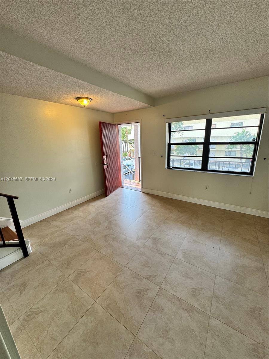 An empty room features beige tile flooring, a textured ceiling, and an open exterior door — 421 Swallow Dr # 10, Miami Springs FL 33166, MIAMI SPRINGS, FL