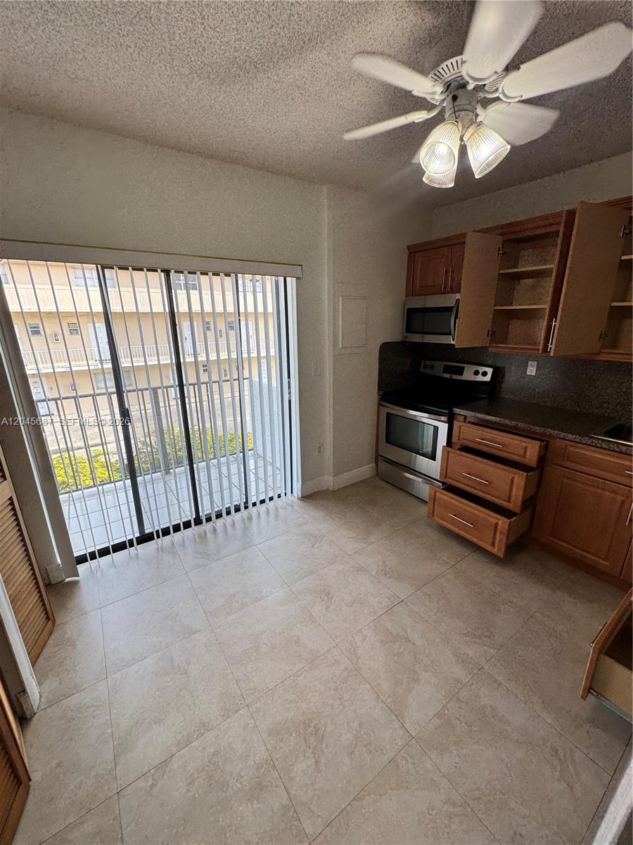 A kitchen with wood cabinets, stainless steel appliances, tile floors, and a sliding glass door — 421 Swallow Dr # 10, Miami Springs FL 33166, MIAMI SPRINGS, FL