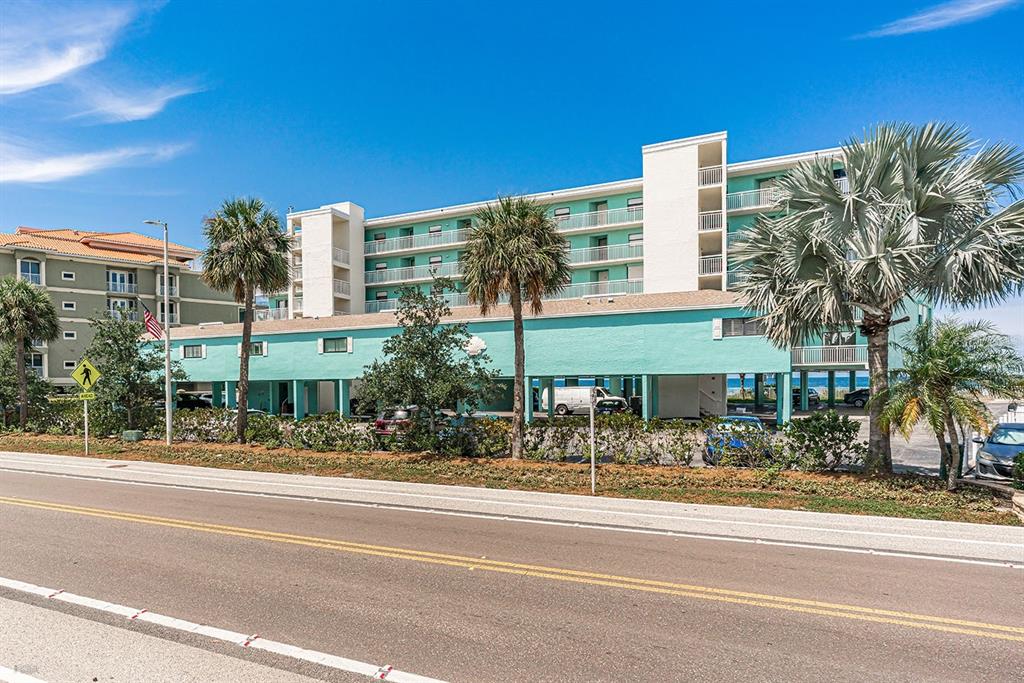 A multi-story turquoise apartment building stands behind a parking area and a paved road — 19440 GULF BOULEVARD UNIT 105, INDIAN SHORES, FL