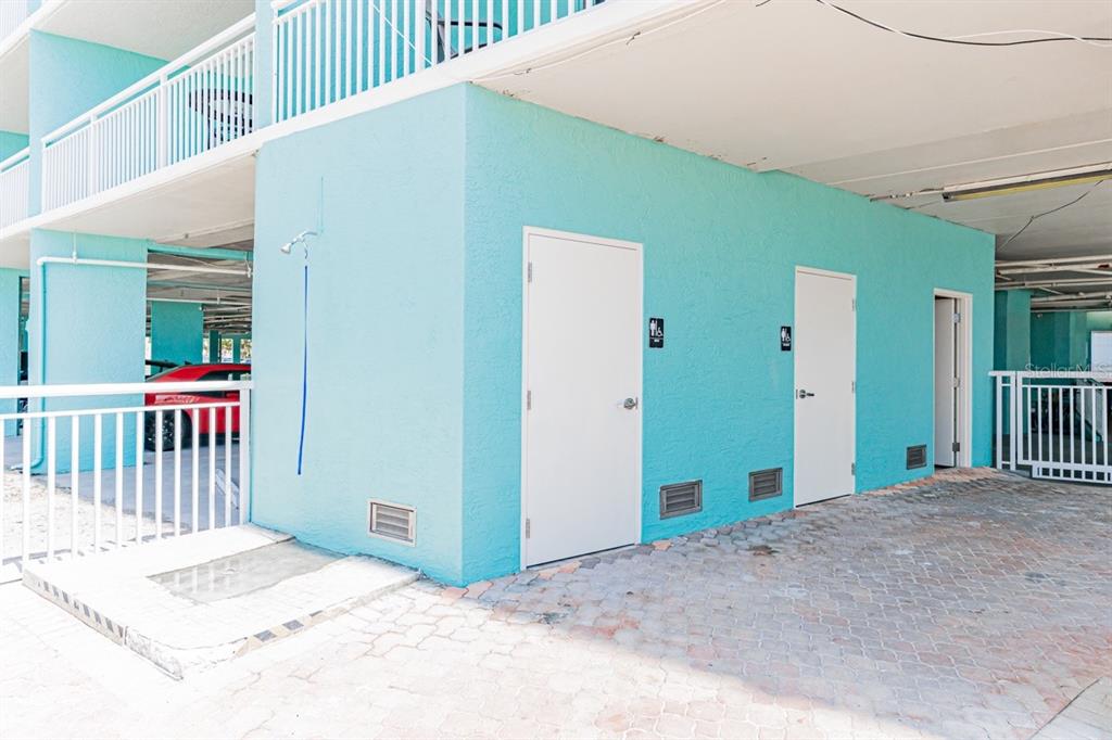 An outdoor area with a shower, two doors with restroom signs, and a paved ground — 19440 GULF BOULEVARD UNIT 105, INDIAN SHORES, FL