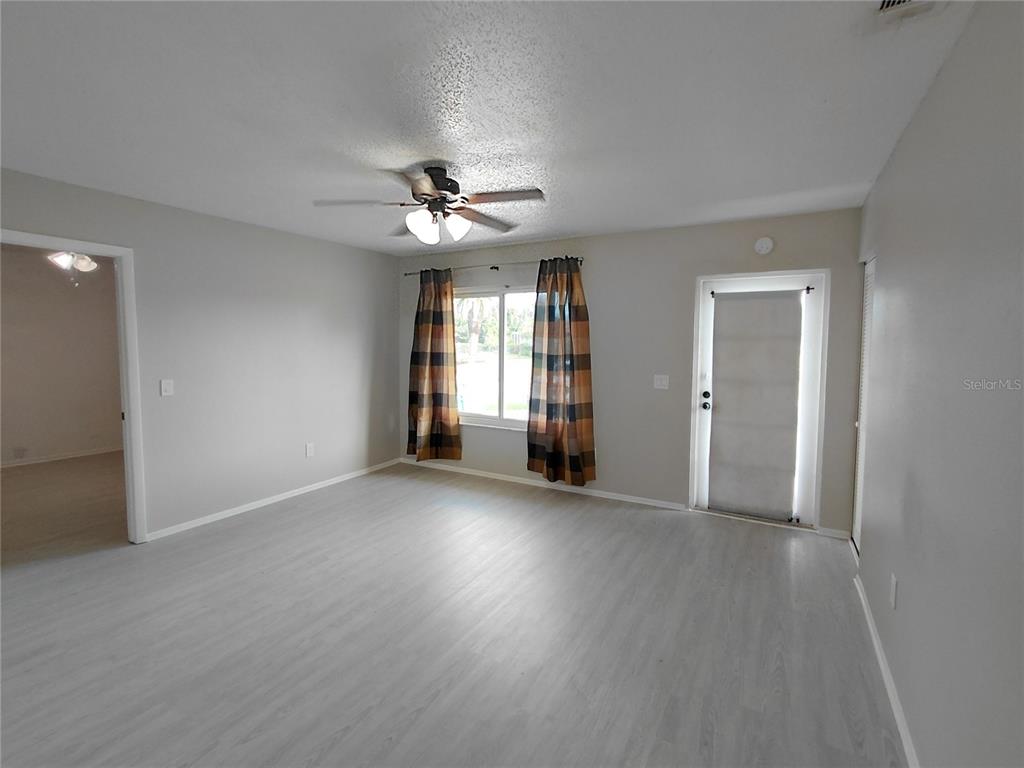 A living room with light gray flooring, a ceiling fan, and a glass-paneled exterior door — 18292 MORRISSON AVENUE, PORT CHARLOTTE, FL