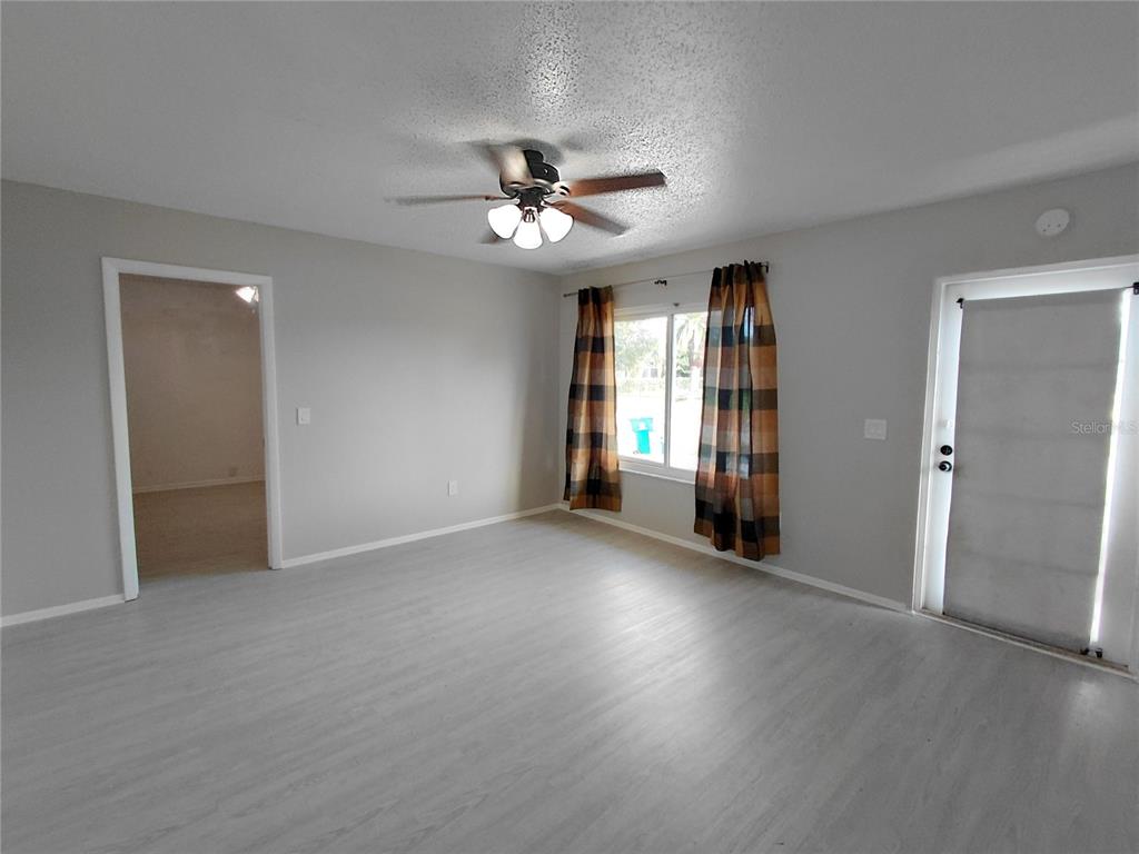 A living room with light gray walls, wood-look flooring, a ceiling fan, and a glass door — 18292 MORRISSON AVENUE, PORT CHARLOTTE, FL