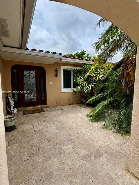 A stone-paved courtyard leads to a dark wooden door with decorative iron grillwork — 9624 SW 79th Ter, Miami FL 33173, MIAMI, FL