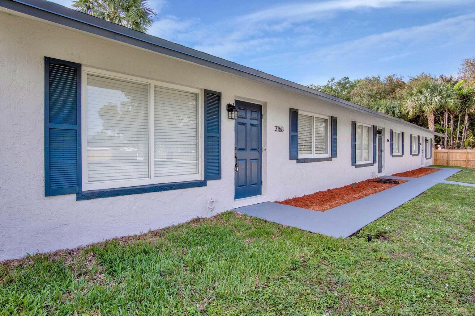 A white single-story building features blue shutters, a blue front door, and a concrete walkway — 3166 Melaleuca Road, West Palm Beach FL 33406, WEST PALM BEACH, FL