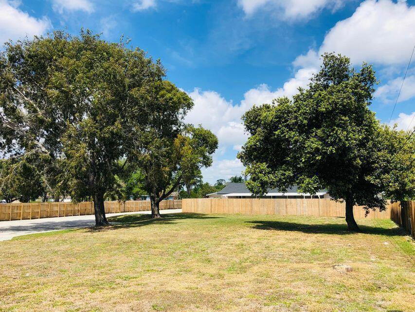 A grassy lot features several large trees and a wooden privacy fence under a blue sky — 3166 Melaleuca Road, West Palm Beach FL 33406, WEST PALM BEACH, FL