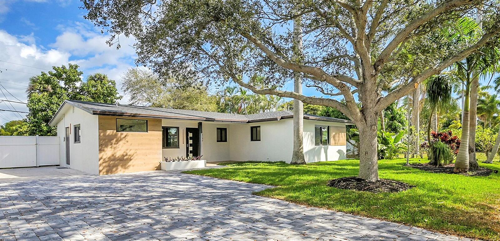 A single-story house with white stucco, wood-look siding, and a paved driveway under a tree — 1257 NW 4th Street, Boca Raton FL 33486, BOCA RATON, FL