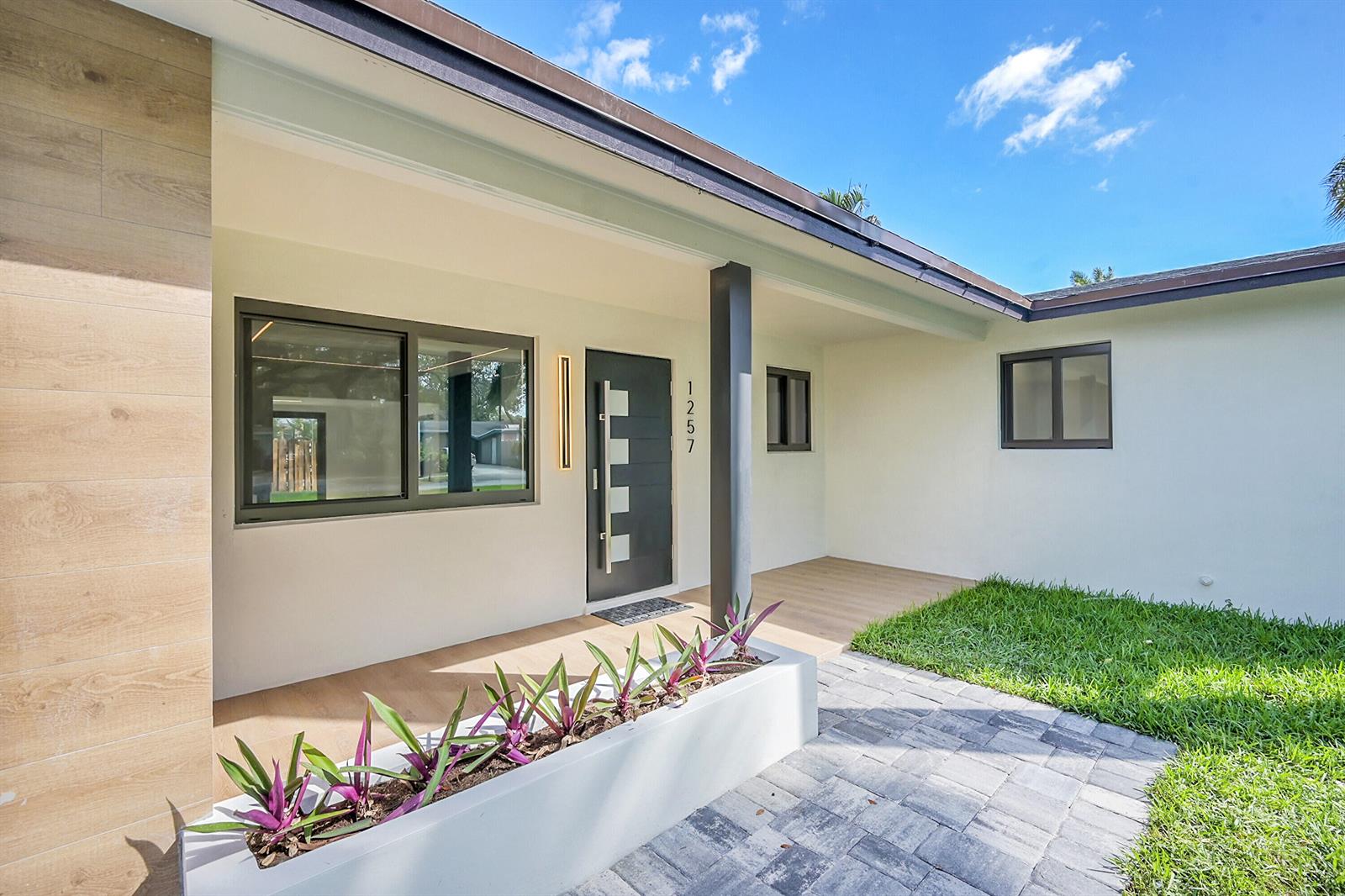 A modern home exterior features a gray front door, a white planter, and wood-look flooring — 1257 NW 4th Street, Boca Raton FL 33486, BOCA RATON, FL