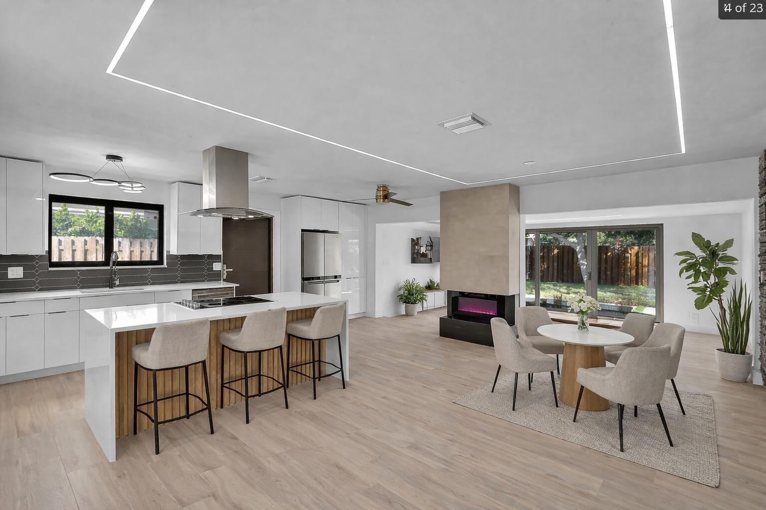 A modern open-concept kitchen and dining area with white cabinetry, a central island, and fireplace — 1257 NW 4th Street, Boca Raton FL 33486, BOCA RATON, FL