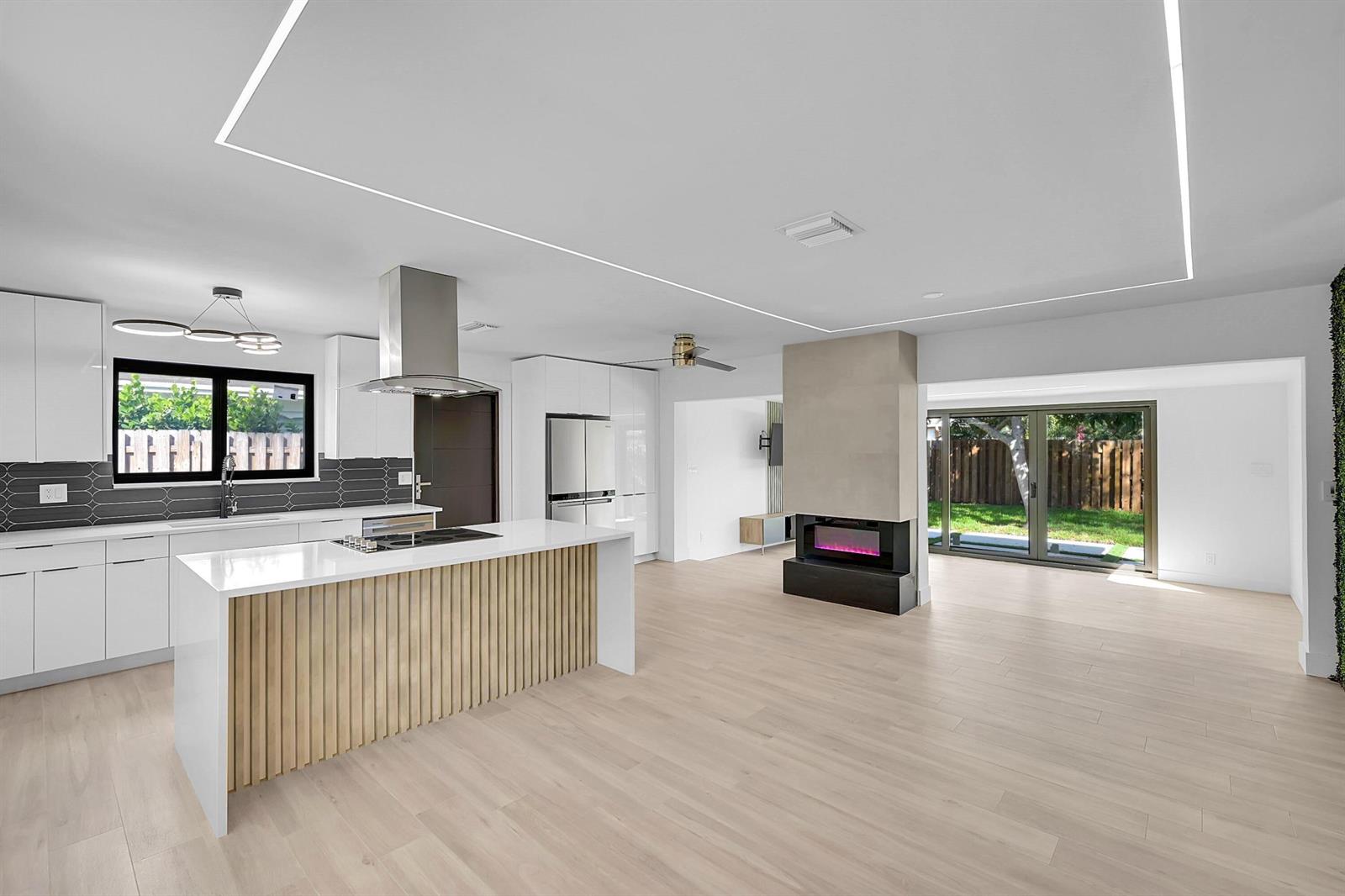 A modern open-concept kitchen and living area features white cabinetry, a slatted island, and fireplace — 1257 NW 4th Street, Boca Raton FL 33486, BOCA RATON, FL